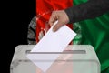 Male voter drops a ballot in a transparent ballot box against the background of the national flag of Afghanistan, concept of state