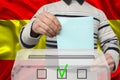 Male voter drops a ballot in a transparent ballot box against the background of the national flag of Spain, concept of state Royalty Free Stock Photo
