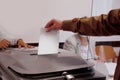 Male voter throws a ballot paper into a gray ballot box at a polling station in Germany, hand with paper close-up, concept of