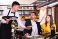 Male waiter is serves an order for smiling couple who is drinking wine and eating Royalty Free Stock Photo