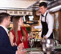 Male waiter is serves an order for smiling couple who is drinking wine and eating Royalty Free Stock Photo