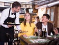 Male waiter is serves an order for smiling couple who is drinking wine and eating Royalty Free Stock Photo