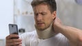 Male wearing cervical collar holding phone suddenly feeling sharp neck pain