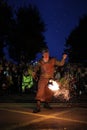 Male wearing a colorful costume and holding a flaming prop performing a fire show