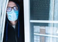 Male wearing glasses and a sanitary face mask while standing behind a window - Pandemic