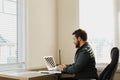 Male web developer sitting at desk and using laptop at cabinet.