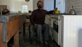 Male in a wheelchair cooking food in the kitchen. He is wearing a face mask