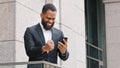 Male winner ethnic bearded African American man entrepreneur businessman looking at mobile phone screen reading message