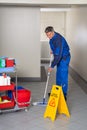 Male Worker With Broom Cleaning Corridor