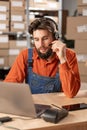 Male worker with headset working in on-site office of a warehouse using laptop computer consulting clients. Royalty Free Stock Photo