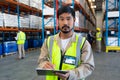 Male worker looking at camera while writing on clipboard in warehouse Royalty Free Stock Photo