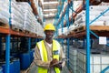 Male worker looking at camera while writing on clipboard in warehouse Royalty Free Stock Photo