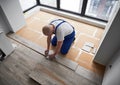 Male worker measuring and marking laminate plank in apartment.