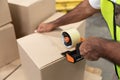 Male worker packing cardboard box with tape gun dispenser in warehouse Royalty Free Stock Photo