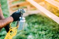 male worker painting brown timber using spray gun and air compressor