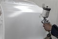 A male worker paints with a spray gun a part of the car body in