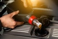 A male worker pours motor oil into a car engine from a gray canister with a red cap under the hood during maintenance and repair.