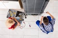 Male Worker Repairing Refrigerator In Kitchen Room