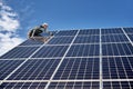 Male worker on solar plant installing solar batteries, standing on a ladder on a sunny day
