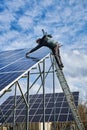 Male worker on solar plant installing solar batteries, standing on a ladder on a sunny day