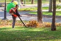 A male worker uses Leaf blower to remove leaves in a park in autumn. Tidying up and preparing the garden for winter