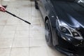 A male worker washes a black car with a high-pressure apparatus from which water flows and washes away foam and chemicals in a veh