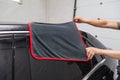 A male worker washes a black car, wiping water with a soft cloth and microfiber, cleaning the surface to shine in a vehicle Royalty Free Stock Photo