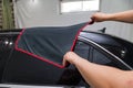 A male worker washes roof of a black car, wiping water with a soft cloth and microfiber, cleaning the surface to shine in a Royalty Free Stock Photo