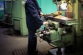 A male worker works on a larger metal iron locksmith lathe, equipment for repairs, metal work in a workshop at a metallurgical