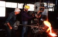 Male workers in a metal work foundry pouring red hot molten metal