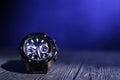 Male wrist watch on table under light beam over dark blue background