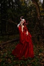 Maleficent Woman in Red Clothing and Horns in dark Forest. Posing in magik forest Royalty Free Stock Photo