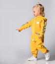 Little cute blonde girl in a warm comfortable overalls standing against a gray wall. Happy childhood and fashionable Royalty Free Stock Photo