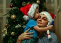 A little boy wearing Santa Claus hat and his uncle wearing Snow Maiden hat sitting on background of New Year tree.