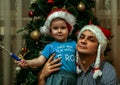 A little boy wearing Santa Claus hat and his uncle wearing Snow Maiden hat sitting on background of New Year tree.