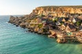 Malta, Il-Mellieha. View of the famous Popeye Village in Anchor Bay. Turquoise sea waters, blue sky and sunset light on cliffs Royalty Free Stock Photo