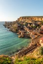 Malta, Il-Mellieha. View of the famous Popeye Village in Anchor Bay. Turquoise sea waters, blue sky and sunset light on cliffs Royalty Free Stock Photo