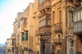 Malta, Valletta, traditional sandstone buildings with colorful wooden windows on balconies. Blue sky with clouds and sea backgroun Royalty Free Stock Photo