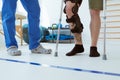 Man after car accident in an orthosis and on crutches learning to walk in the clinic, helpful therapist near him Royalty Free Stock Photo