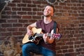 Man with acoustic guitar against brick wall playing music singing songs enjoy life Medium shoot