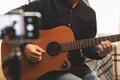 Man with acoustic guitar in a shirt and cap plays live staying home for the audience in front of the smartphone camera during