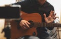 Man with acoustic guitar in a shirt and cap plays live staying home for the audience in front of the smartphone camera during