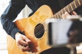 Man with acoustic guitar in a shirt and cap plays live staying home for the audience in front of the smartphone camera during