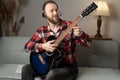 Man with acoustic guitar sitting on sofa wearing headphones. Caucasian guitar player practicing playing on musical Royalty Free Stock Photo