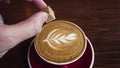 Man add a brown sugar cube into the hot latte coffee with froth art on top of milk froth slomo