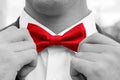 Man adjusts red bow tie with hands. Black and white photo with coloured element.