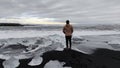 Man admiring the view of sea with foamy waves crashing on a black sandy beach with small icebergs Royalty Free Stock Photo