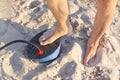 A Man with air foot pump pumps an inflatable mattress or air bed at sandy beach. Foot inflates air mattress with foot Royalty Free Stock Photo