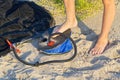 A Man with air foot pump pumps an inflatable mattress or air bed at sandy beach. Foot inflates air mattress with foot Royalty Free Stock Photo