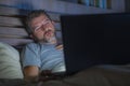 Man alone in bed playing cybersex using laptop computer watching sex movie late at night with lascivious pervert face Royalty Free Stock Photo